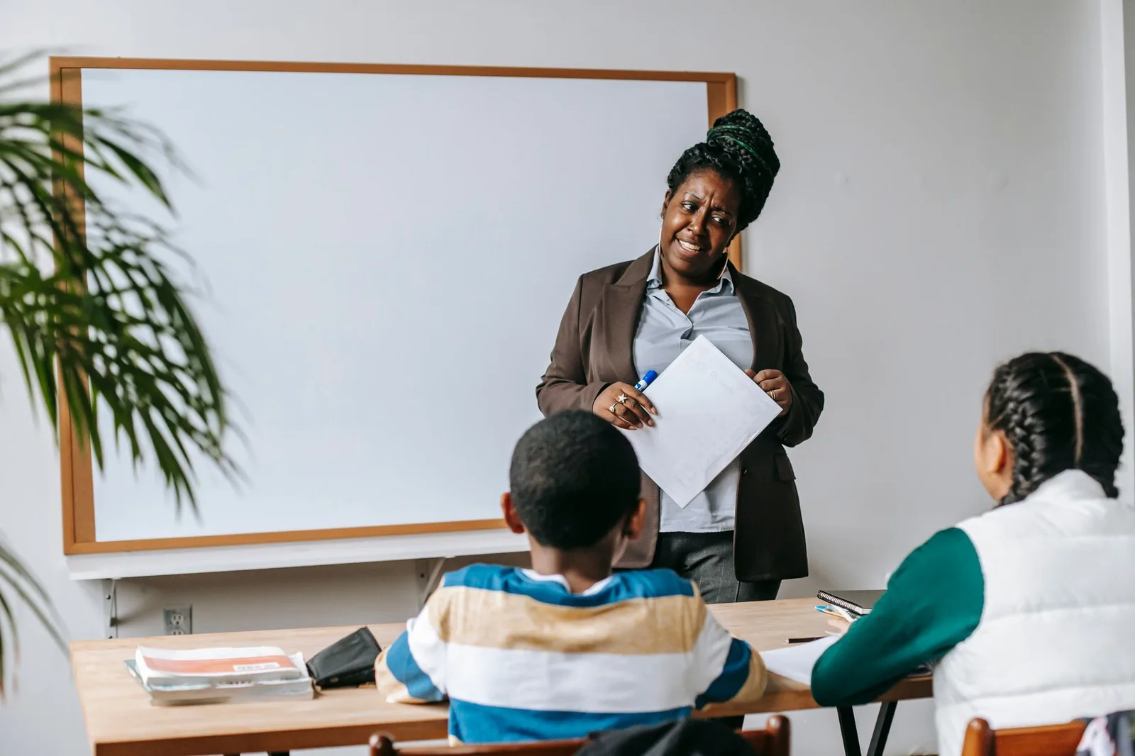 Back view of diverse school children communicating with African American woman against whiteboard in classroom