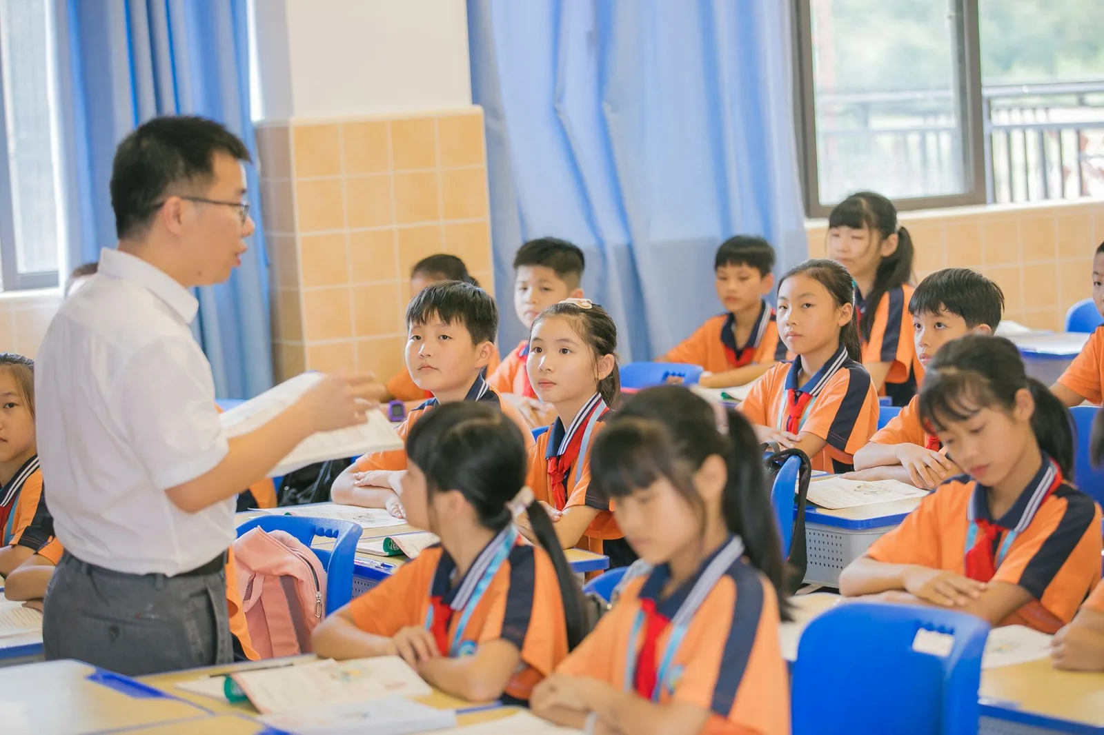 Asian teacher conducting a lesson with attentive students in a bright classroom setting.
